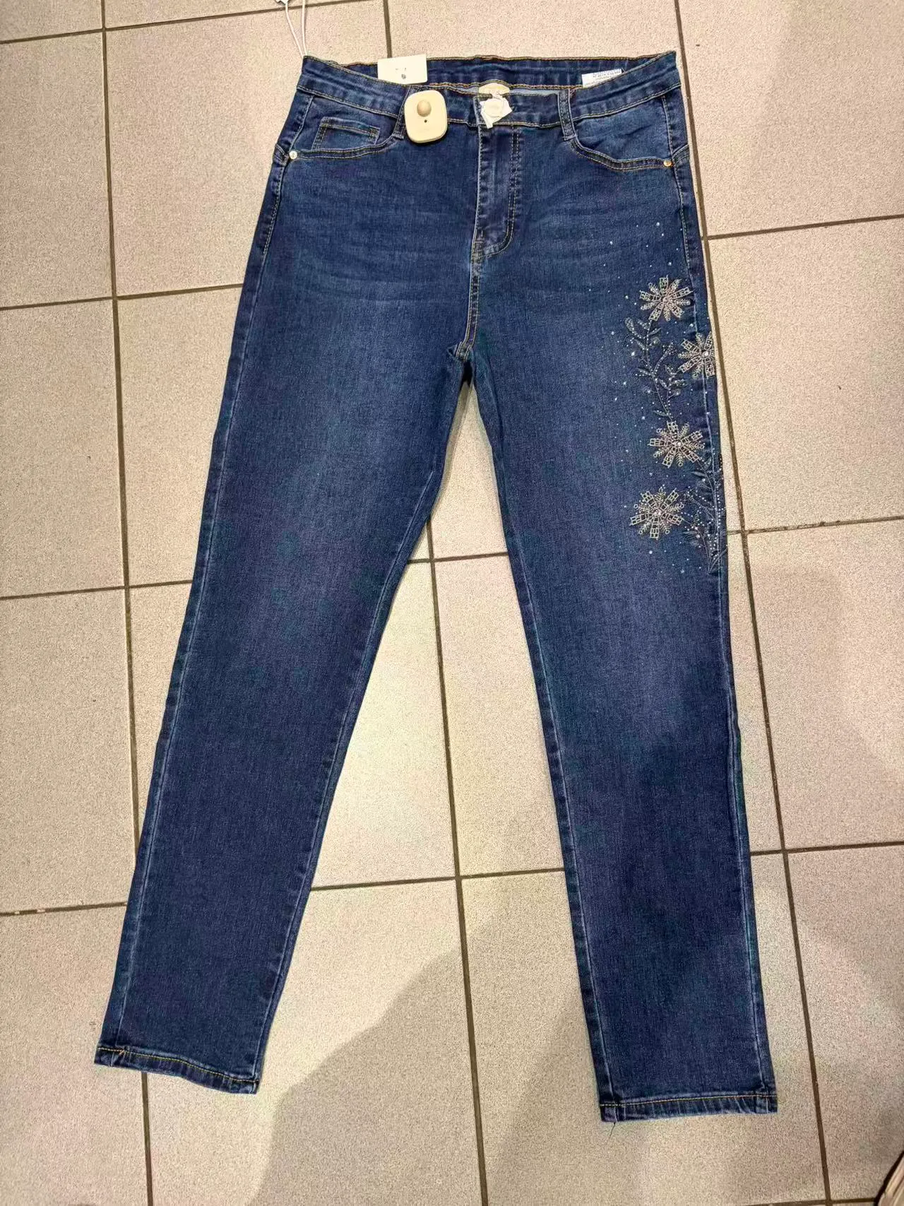 Jeans slim blu con ricamo floreale e dettagli luminosi su una gamba, vista frontale